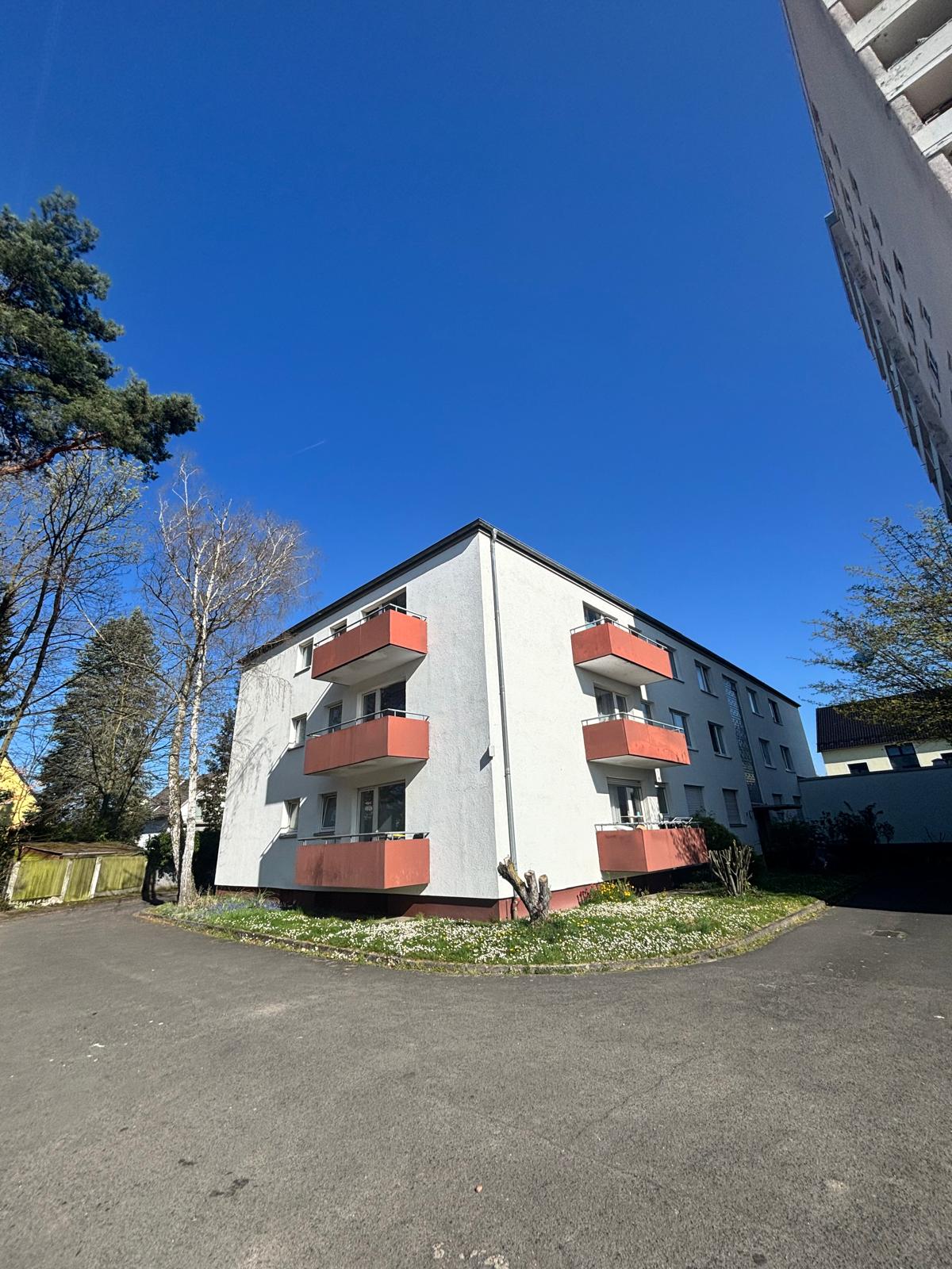 Mehrfamilienhaus mit rot abgesetzten Balkonen und gepflegter Grünfläche